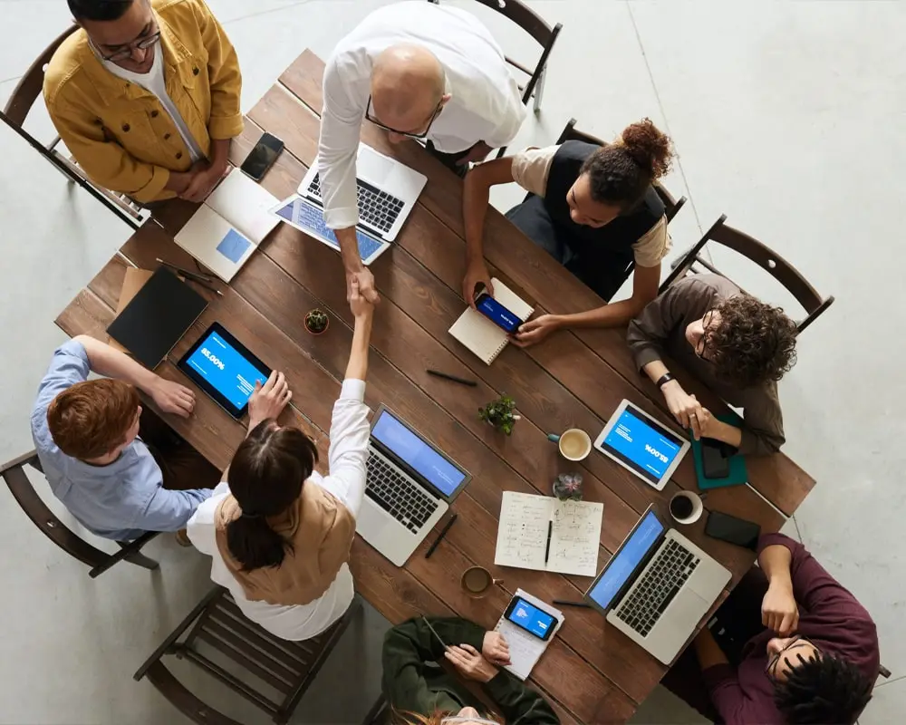 An overhead view of multiple individuals seated around a large table, exchanging handshakes in a professional setting, signifying successful agreements, teamwork, and collaborative decision-making.